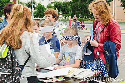 HORKI, BELARUS - JULY 25, 2018: Small blindfolded boys draw on paper on a table on a summer day in a crowd Editorial Stock Photo