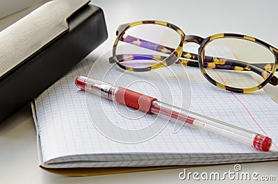 Horn-rimmed glasses, red ink pen and glasses case on a checkered notebook Stock Photo