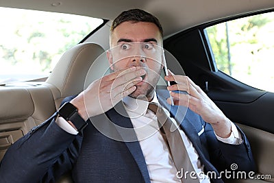 Horrified businessman stressed out in backseat holding mobile phone Stock Photo