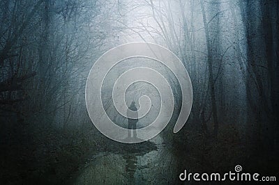 A horror concept of a figure standing by a woodland stream in a forest in winter. With a grunge, artistic, edit Stock Photo