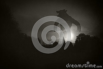 A horror concept.. Of a giant werewolf, standing above a house and countryside at night. With a grunge, textured edit Stock Photo