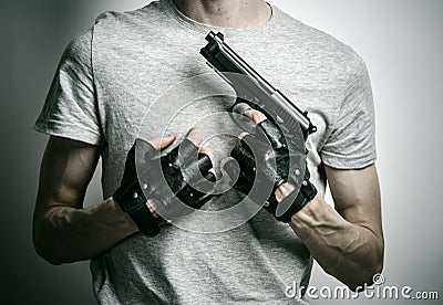 Horror and firearms topic: the killer with a gun in his hand in black gloves on a gray background in the studio Stock Photo