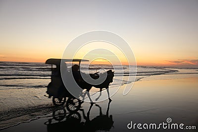A horse-drawn carriage with a group of people driving in very close distance at sunset time on a wet and reflecting beach sand Stock Photo