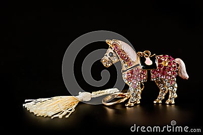 Horse figurine souvenir keychain in gold color ornate with bright pebbles shot on a dark background Stock Photo