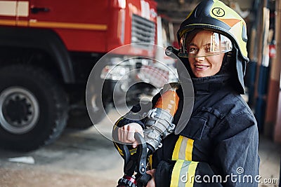 Hose in hands. Female firefighter in protective uniform standing near truck Stock Photo