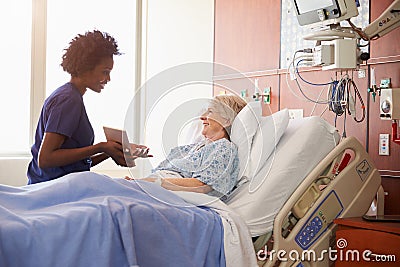 Hospital Nurse With Digital Tablet Talks To Senior Patient Stock Photo