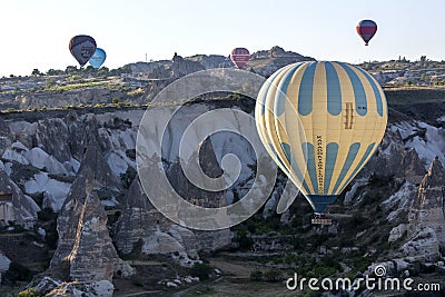 A hot air balloon flies down Love Valley at sunrise near Goreme in the Cappadocia region of Turkey. Editorial Stock Photo