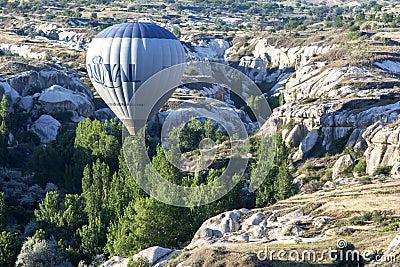 A hot air balloon flies down Love Valley at sunrise near Goreme in the Cappadocia region of Turkey. Editorial Stock Photo