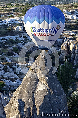 A hot air balloon flies past a fairy chimney at sunrise near Goreme in the Cappadocia region of Turkey. Editorial Stock Photo