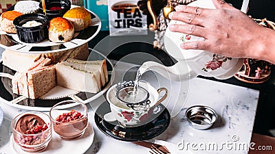 Hot Butterfly Pea Blueberry Tea served by pouring from mug through stainless steel tea strainer infuser in porcelain vintage cup Stock Photo