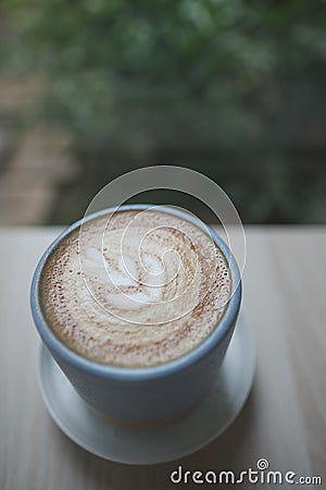 Hot cappuccino coffee cup with tree shape latte art milk foam on wood table near window in garden at cafe restaurant Stock Photo