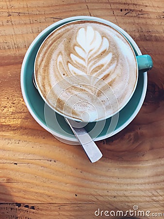 Hot Cappuccino coffee decorated with Tree Leaves on Milk Latte Foam Froth art in blue mug cup on rustic wooden table background. Stock Photo