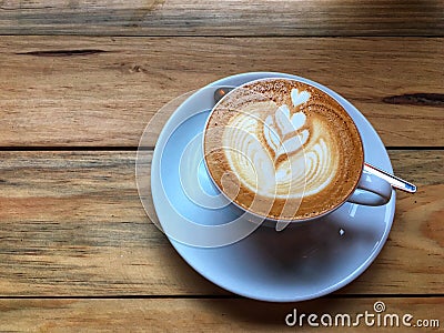 Hot cappuccino coffee in white cup and saucer with spoon on wooden table background. Art of milk foam drawing. Stock Photo