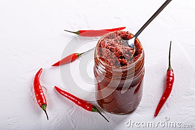 Hot chili pepper paste. Red sauce in glass jar on white background. Adjika or ajika in Georgian cuisine or harissa in Arabic Stock Photo