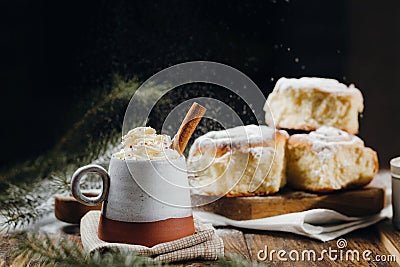 A hot cocoa with whipped cream, cinnamon stick and fresh Christmas buns with powder and over festive table, sugar powder is Stock Photo