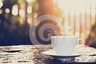 Hot coffee on old wood table with blur background of sunlight shining through the trees Stock Photo