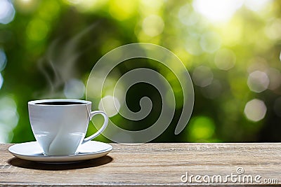 Hot cup of coffee on wooden tabletop on blurred green nature bokeh background Stock Photo