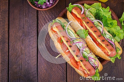 Hot dog with sausage, cucumber, tomato and lettuce on dark wooden background. Stock Photo