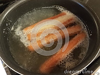 Hot dogs cooking in water in pot on stove Stock Photo