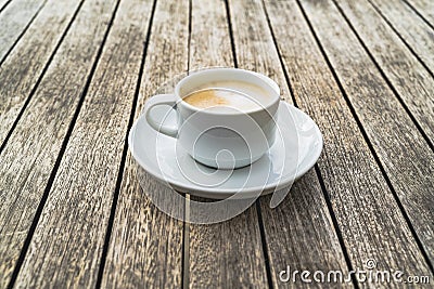 Hot foaming cappuccino in a white ceramic cup on a saucer stands on a table of wooden boards Stock Photo