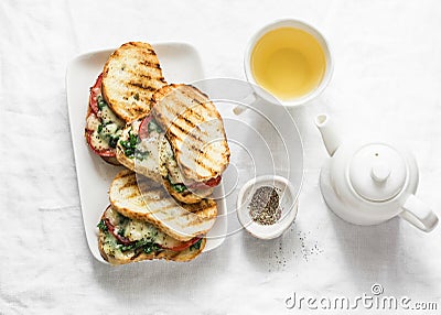 Hot grilled tomatoes, spinach, mozzarella sandwiches and green tea - healthy breakfast, snack on a light background Stock Photo