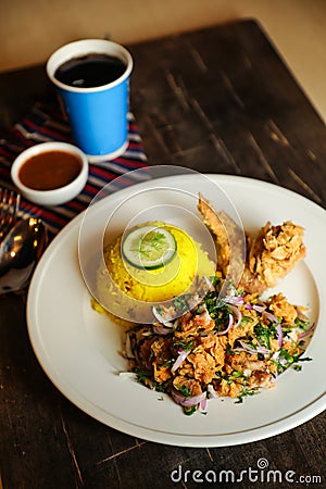 Hot Lemony Chicken Rice Meal served in plate with sauce, cold drink, spoon and fork isolated on wooden board side view of thai Stock Photo