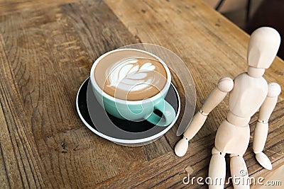 Hot mocha coffee or capuchino in the green cup with a wood man sitting on the wooden table Stock Photo