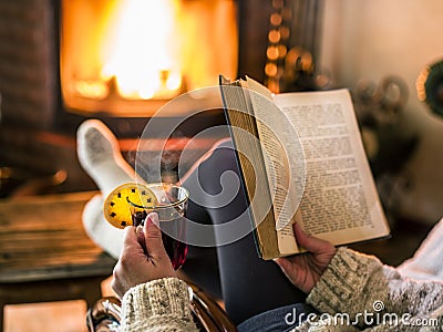 Hot mulled wine and book in woman hands. Relaxing in front of burning fire in the cold winter day Stock Photo