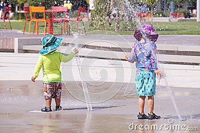 Colorful children dressed in streams of water from the fountain. Hot summer Editorial Stock Photo