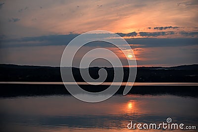 Hot sunset above the forest. Refelctions of red clouds in the water of the lake. bright colors at the end of a summer day Stock Photo