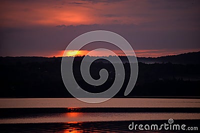 Hot sunset above the forest. Refelctions of red clouds in the water of the lake. bright colors at the end of a summer day Stock Photo