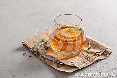 Hot tea in a glass with lemon and thyme on a linen napkin, gray background with copy space. Autumn and winter traditional drinks Stock Photo