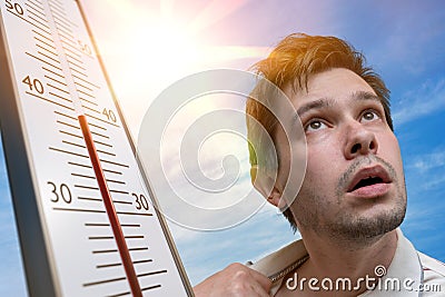 Hot weather concept. Young man is sweating. Thermometer is showing high temperature. Sun in background Stock Photo