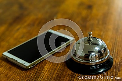 Hotel service call bell and smartphone on wooden reception front Stock Photo