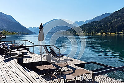 Hotel terrace with deck chairs on the shores of an alpine lake surrounded by mountains Stock Photo