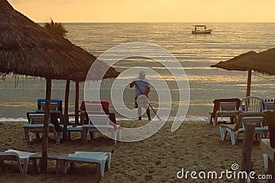 Hotel worker cleans the beach against the sea in the rays of the golden dawn Editorial Stock Photo