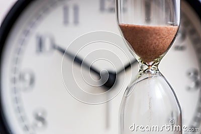 Hourglass on the background of office watch as time passing concept for business deadline, urgency and running out of time. Sand Stock Photo