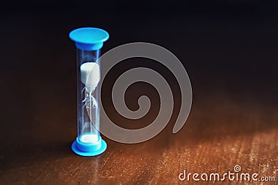 Hourglass blue color, white sand on dark background Stock Photo