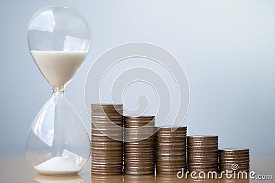Hourglass blue sand and stack of coins. Stock Photo