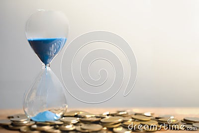 Hourglass blue sand and stack of coins. Stock Photo