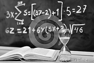 Hourglass and book on a table, with a blackboard background Stock Photo