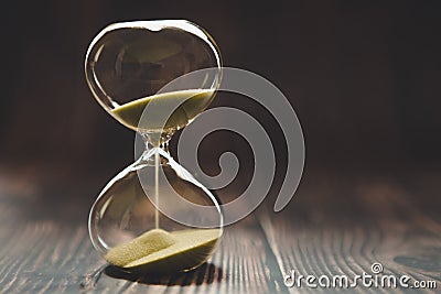 Hourglass with falling sand inside a glass bulb, passing time or lost time on a dark background with space for text Stock Photo