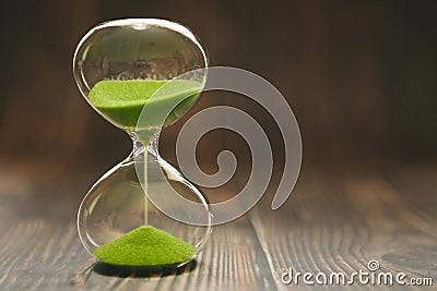 Hourglass with falling sand inside a glass bulb, passing time or lost time on a wooden background with space for text Stock Photo