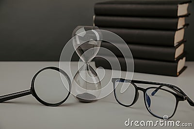 Hourglass with glasses, magnifier and books on a desk Stock Photo
