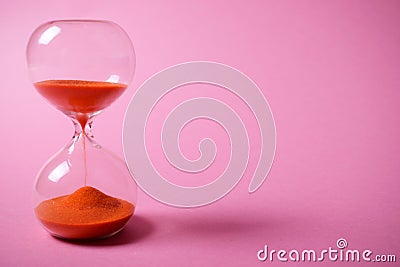 Hourglass with orange sand on pink background. Stock Photo