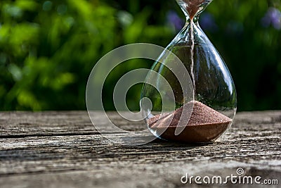 Hourglass with pouring sand against a background of blurred greenery. The bottom of the glass flask Stock Photo
