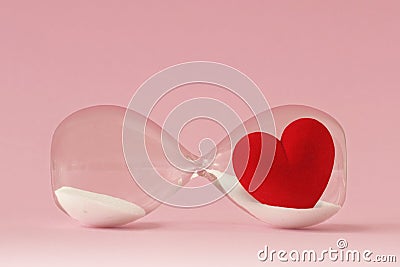 Hourglass stopped flowing with heart on pink background - Concept of time and love Stock Photo