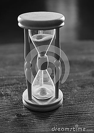 Hourglass on wooden table, dark background. Sand falling down inside of hourglass. Time flow concept. Wooden hourglass Stock Photo