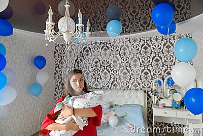 HOUSE AFTER BIRTH. decorated room for a young mother. surprise at home. Mother holds her baby in her arms in a white bedroom. Love Stock Photo
