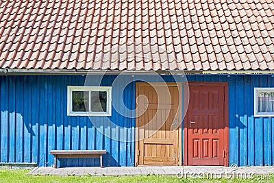 House of blue wooden planks, red roof, two colorful doors and small windows Stock Photo